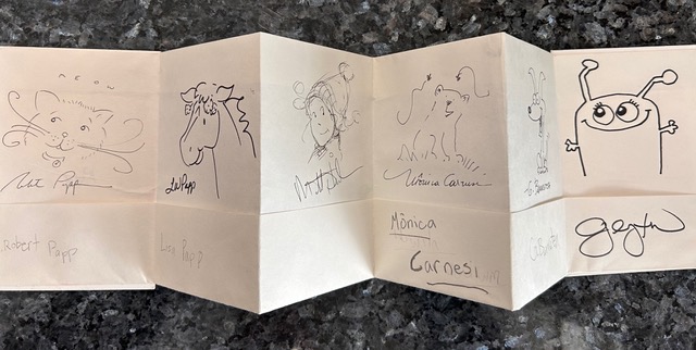 accordion folded booklet with illustrations and signatures from illustrators who participated in the event "From Shelves to Studios": Robert Papp, Lisa Papp, Monica Carnesi, and more.